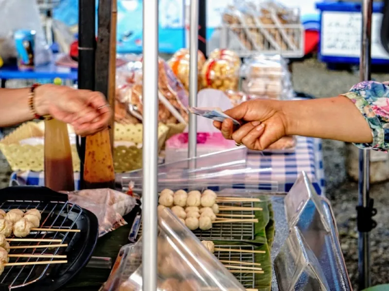Woman handing over cash to a seller on a local market after buying some local food